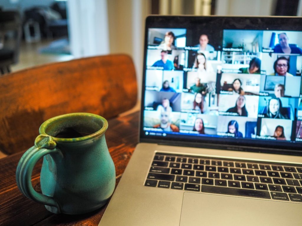 Laptop showing a large Zoom video call grid with a coffee mug in the foreground, representing remote team communication