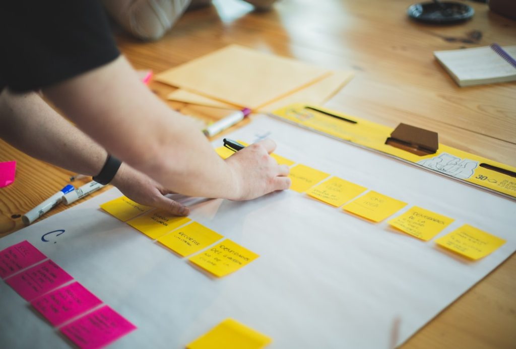 Person organizing colorful sticky notes on a large planning sheet, mapping out tasks and workflow for a project